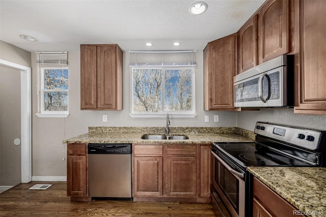 kitchen with visible vents, dark wood-type flooring, a sink, light stone counters, and appliances with stainless steel finishes