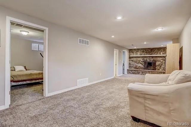 living area featuring a stone fireplace, carpet flooring, baseboards, and visible vents