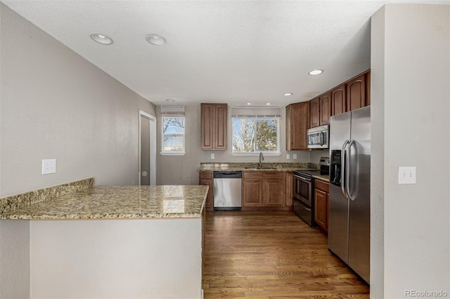 kitchen featuring dark wood-type flooring, a sink, appliances with stainless steel finishes, a peninsula, and light stone countertops