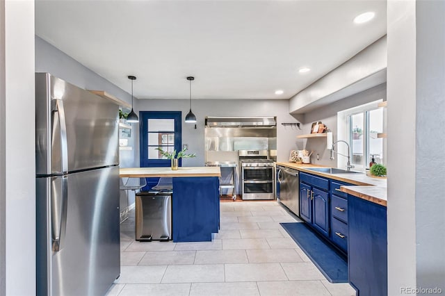 kitchen featuring pendant lighting, sink, blue cabinetry, appliances with stainless steel finishes, and butcher block counters