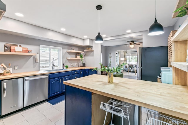 kitchen with blue cabinetry, wood counters, sink, decorative light fixtures, and appliances with stainless steel finishes