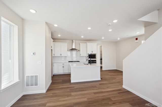 kitchen featuring a center island with sink, dark hardwood / wood-style floors, white cabinets, wall chimney range hood, and backsplash