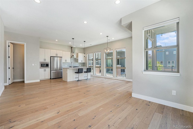 5018 S Prince Pl, Littleton, CO 80123 - kitchen featuring appliances with stainless steel finishes, wall chimney range hood, a breakfast bar, white cabinets, and healthy amount of natural light