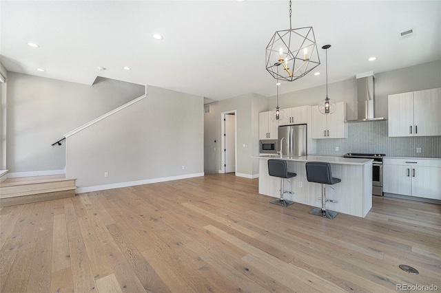 5018 S Prince Pl, Littleton, CO 80123 - kitchen with wall chimney range hood, appliances with stainless steel finishes, a breakfast bar, light wood-style flooring, and an island with sink