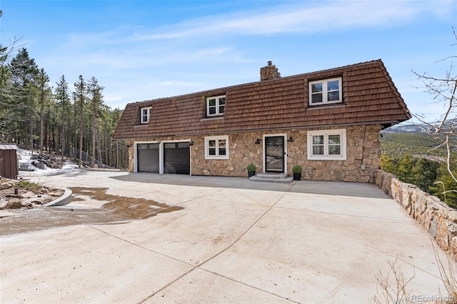 8451 London Ln, Conifer, CO 80433 - view of front property featuring mansard roof, a chimney, a garage, driveway, and stone siding