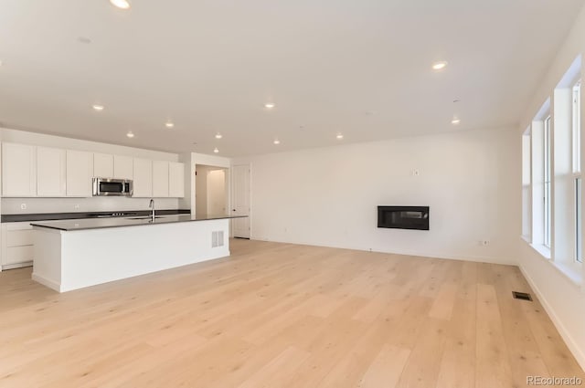 interior space with light hardwood / wood-style flooring, white cabinets, an island with sink, and sink