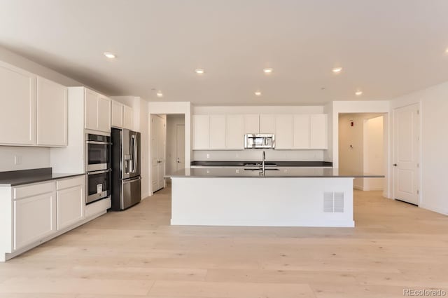 kitchen with white cabinets, a center island with sink, sink, light hardwood / wood-style floors, and stainless steel appliances