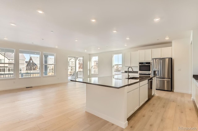 kitchen featuring white cabinetry, sink, stainless steel appliances, a center island with sink, and light wood-type flooring