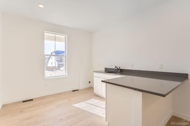 kitchen featuring sink, light hardwood / wood-style flooring, kitchen peninsula, a breakfast bar area, and white cabinets