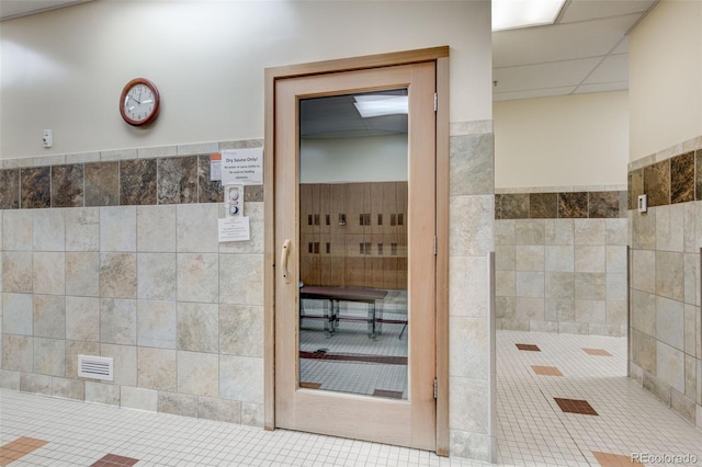 bathroom featuring a paneled ceiling and tile walls