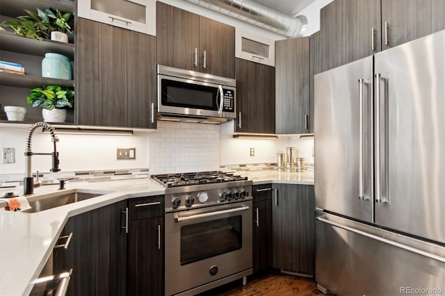 kitchen featuring high end appliances, dark wood-type flooring, sink, and tasteful backsplash