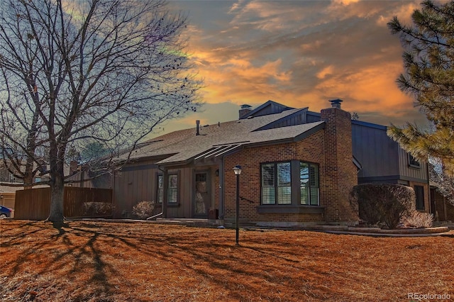 view of front of home featuring a shingled roof, a chimney, fence, and brick siding