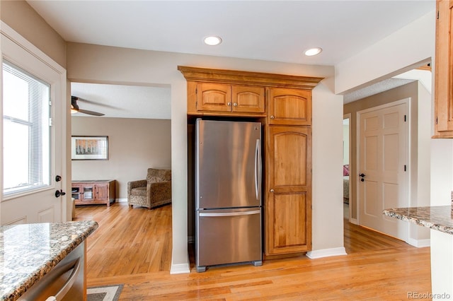 kitchen featuring light stone counters, freestanding refrigerator, brown cabinetry, and light wood-style floors