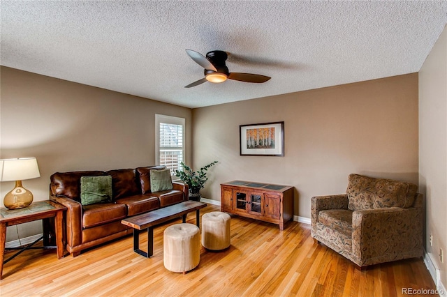 living room featuring light wood-type flooring, ceiling fan, a textured ceiling, and baseboards