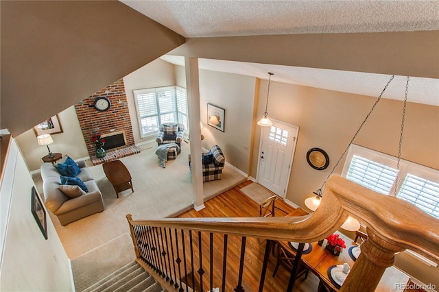 stairway with baseboards, a textured ceiling, carpet floors, a brick fireplace, and high vaulted ceiling