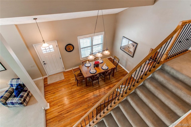 dining space featuring baseboards, high vaulted ceiling, stairway, and light wood-style floors