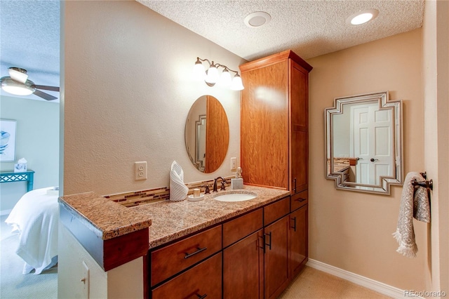 ensuite bathroom with a ceiling fan, connected bathroom, a textured ceiling, vanity, and baseboards