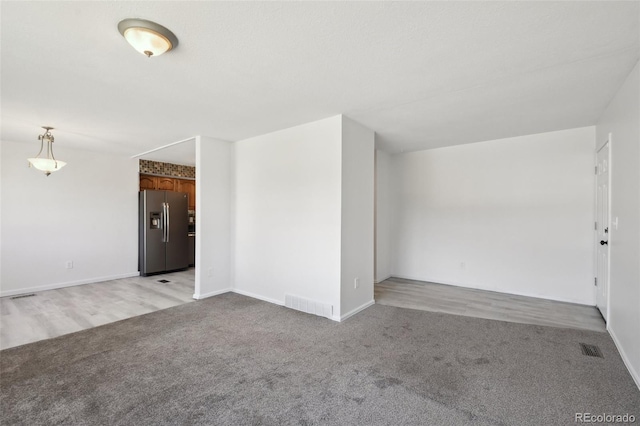 empty room featuring visible vents, light colored carpet, and baseboards