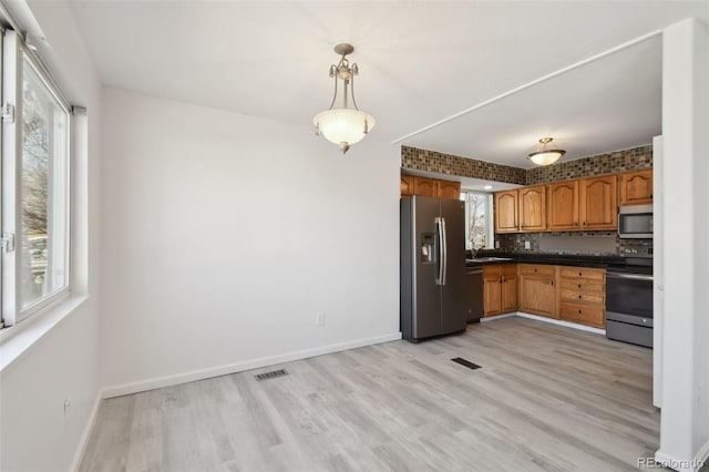 kitchen with visible vents, brown cabinets, dark countertops, stainless steel appliances, and light wood-style floors