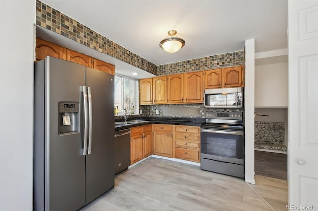 kitchen with dark countertops, backsplash, light wood-style flooring, appliances with stainless steel finishes, and a sink