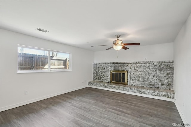 unfurnished living room featuring visible vents, a ceiling fan, wood finished floors, a glass covered fireplace, and baseboards