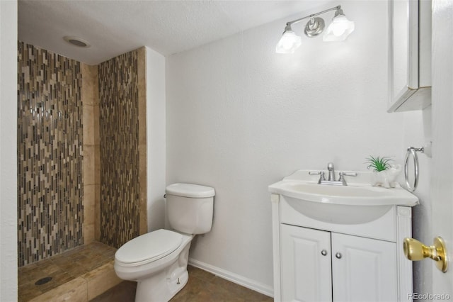 bathroom featuring tile patterned floors, toilet, tiled shower, baseboards, and vanity