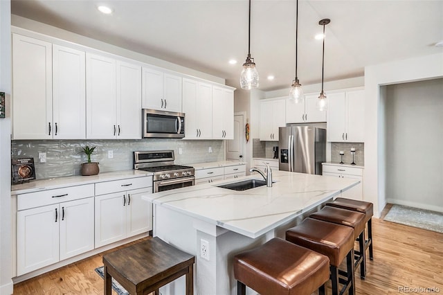 kitchen with a kitchen breakfast bar, light wood-type flooring, a sink, stainless steel appliances, and a center island with sink