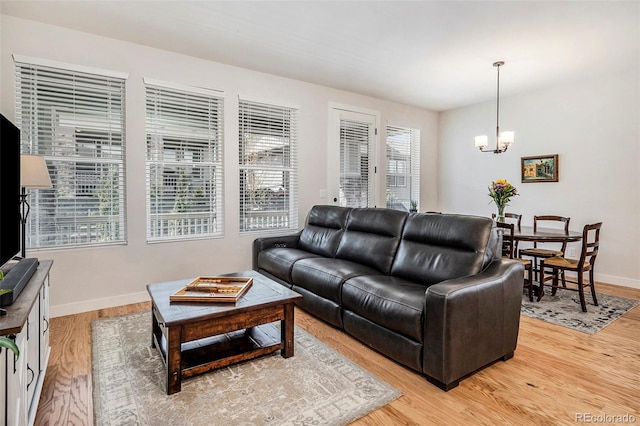 living area featuring light wood-style floors, a notable chandelier, and baseboards