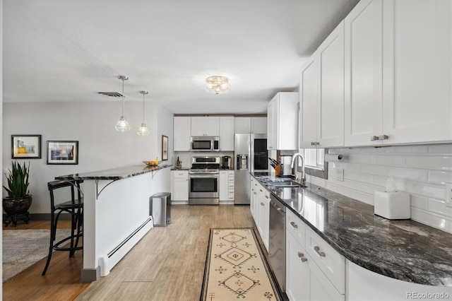 kitchen featuring sink, decorative light fixtures, a baseboard heating unit, stainless steel appliances, and white cabinets