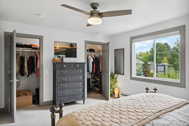 bedroom featuring a walk in closet, a baseboard heating unit, light colored carpet, and ceiling fan