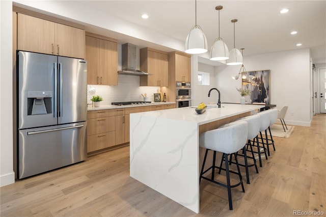 2060 Eliot St, Denver, CO 80211 - kitchen with appliances with stainless steel finishes, wall chimney range hood, light brown cabinetry, recessed lighting, and light wood-type flooring