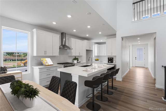 8863 Springsong Ln, Littleton, CO 80125 - kitchen with wall chimney exhaust hood, recessed lighting, wood finished floors, a breakfast bar area, and a kitchen island with sink