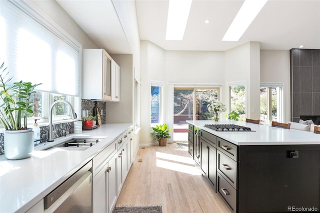 kitchen featuring stainless steel appliances, white cabinets, sink, light hardwood / wood-style flooring, and a skylight