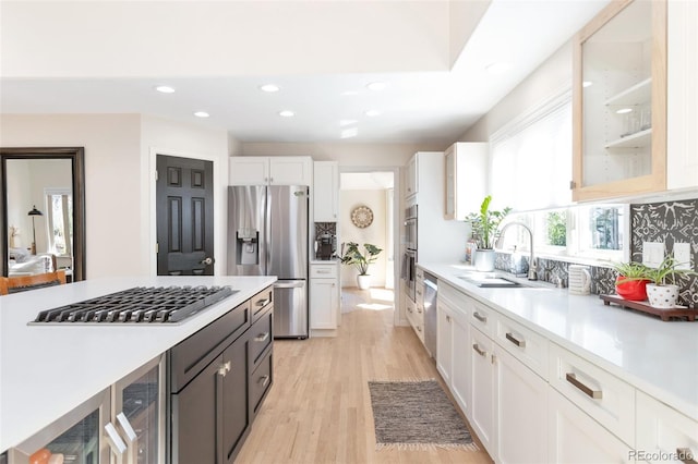 kitchen featuring stainless steel appliances, white cabinets, sink, light hardwood / wood-style flooring, and wine cooler