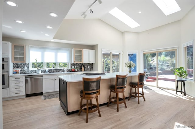 kitchen with plenty of natural light, a skylight, a kitchen island, stainless steel appliances, and white cabinets