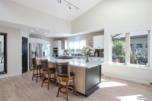 kitchen featuring high vaulted ceiling, white cabinetry, appliances with stainless steel finishes, a center island, and light hardwood / wood-style floors