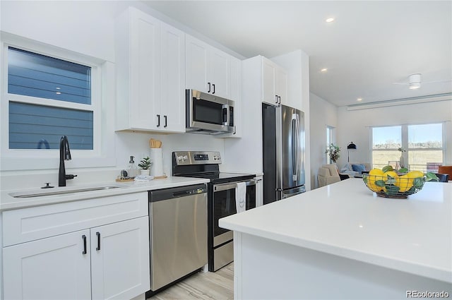 kitchen with light wood-type flooring, stainless steel appliances, white cabinetry, and sink