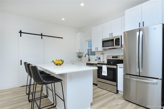 kitchen featuring white cabinets, appliances with stainless steel finishes, light hardwood / wood-style flooring, and a kitchen island