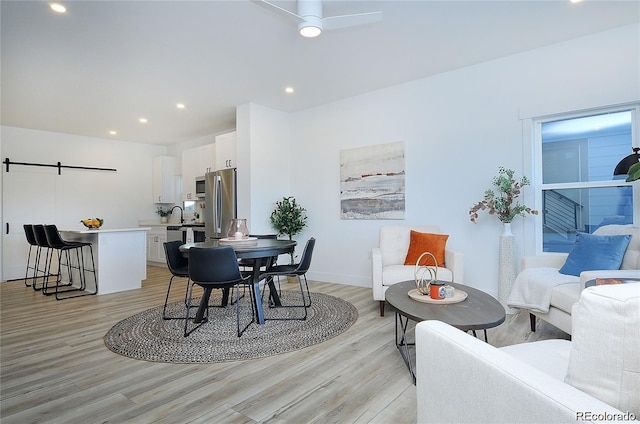 dining space featuring ceiling fan, a barn door, light wood-type flooring, and sink