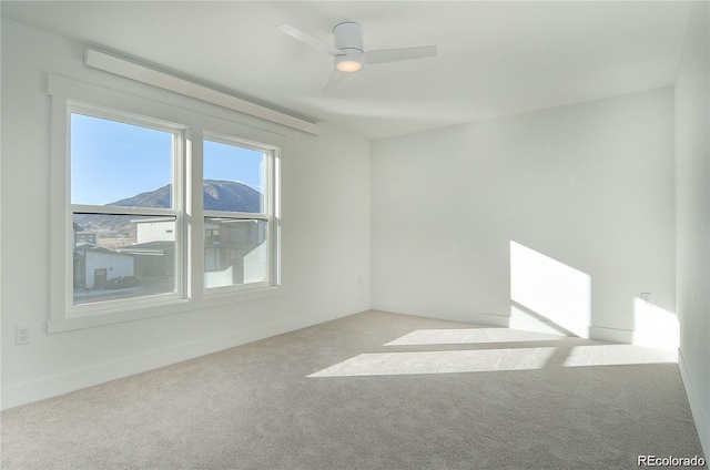 unfurnished room featuring a mountain view, light colored carpet, and ceiling fan