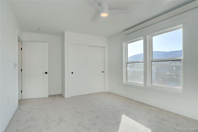 unfurnished bedroom featuring a mountain view, light carpet, a closet, and ceiling fan