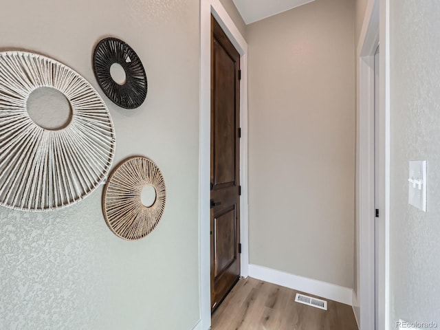 hall with baseboards, visible vents, and wood finished floors