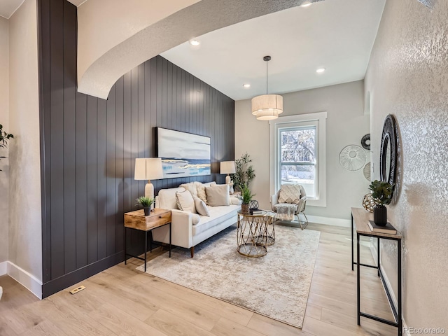 sitting room featuring arched walkways, light wood-style flooring, recessed lighting, an accent wall, and baseboards