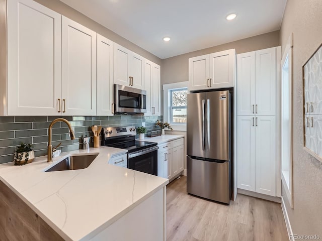 kitchen with appliances with stainless steel finishes, white cabinets, a sink, and light stone counters