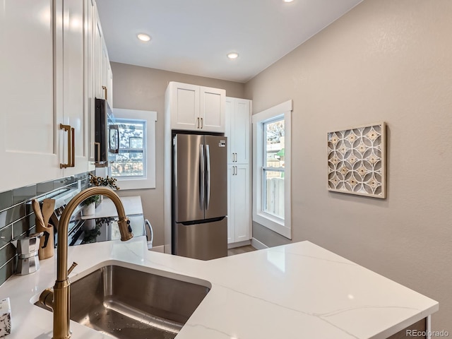 kitchen featuring stainless steel appliances, white cabinetry, a sink, and light stone counters