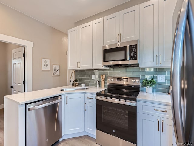 kitchen with decorative backsplash, appliances with stainless steel finishes, a peninsula, light countertops, and a sink