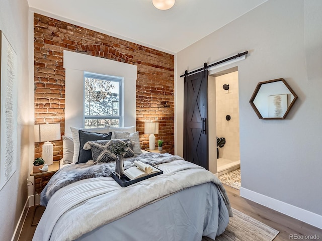 bedroom with a barn door, baseboards, brick wall, wood finished floors, and ensuite bathroom