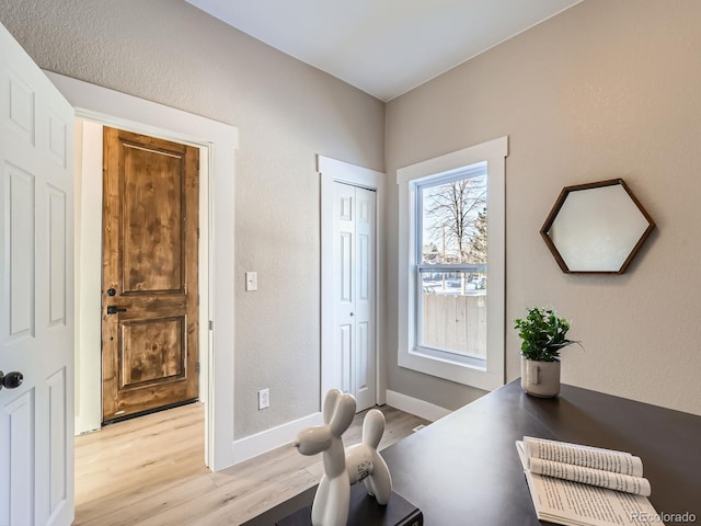 home office with a textured wall, light wood finished floors, and baseboards