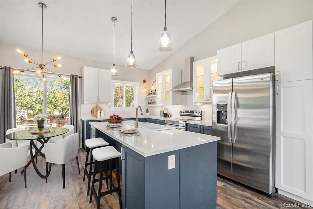 kitchen featuring lofted ceiling, wall chimney exhaust hood, stainless steel appliances, backsplash, and white cabinetry