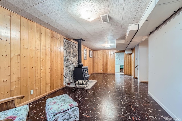 basement featuring a wood stove, a drop ceiling, and wooden walls